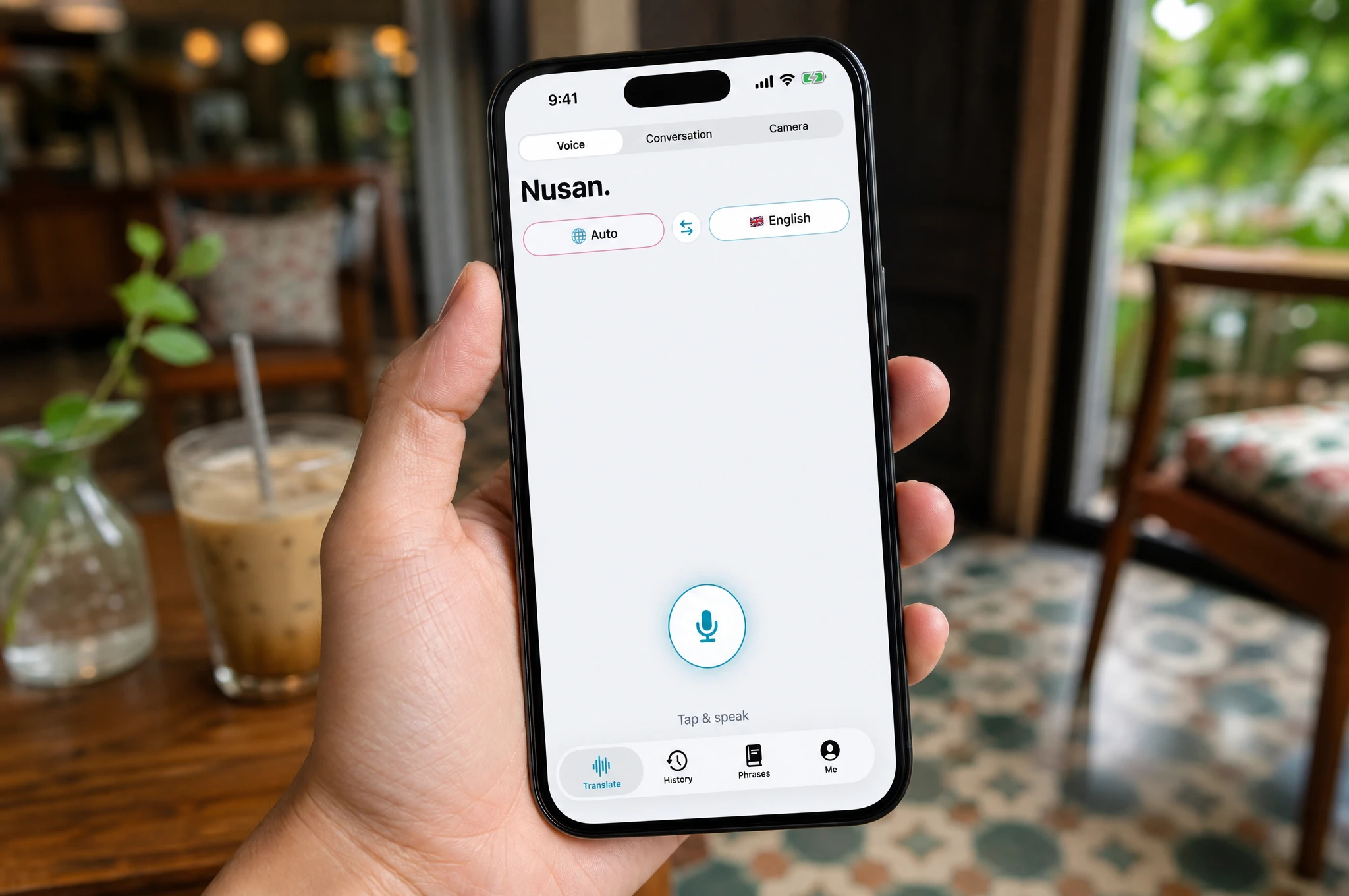 Hand holding a smartphone in a cafe, showing the Nusan voice translation app ready to listen