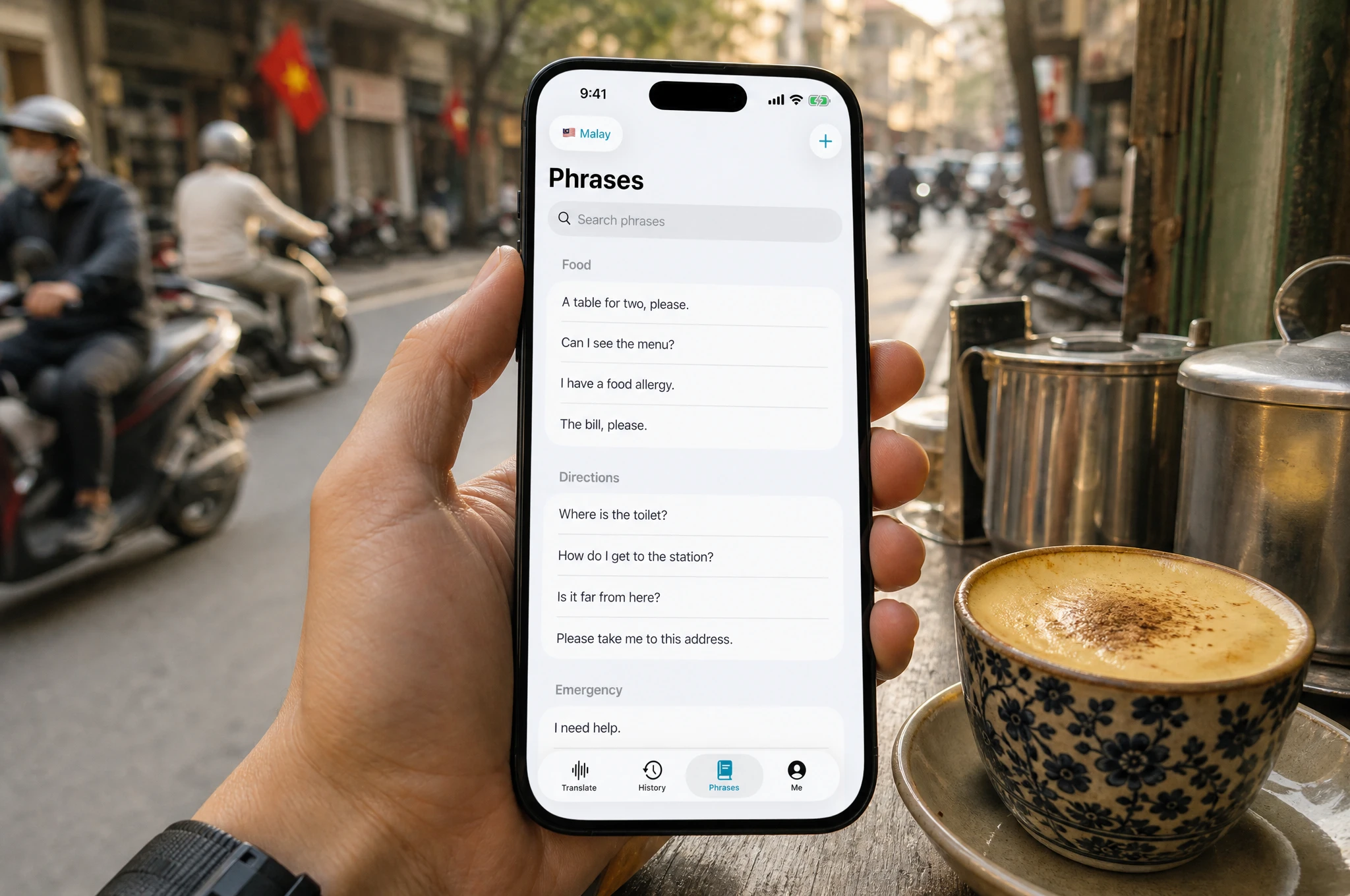 Hand holding a smartphone at a Hanoi street coffee stall, showing the Nusan phrasebook with essential travel phrases