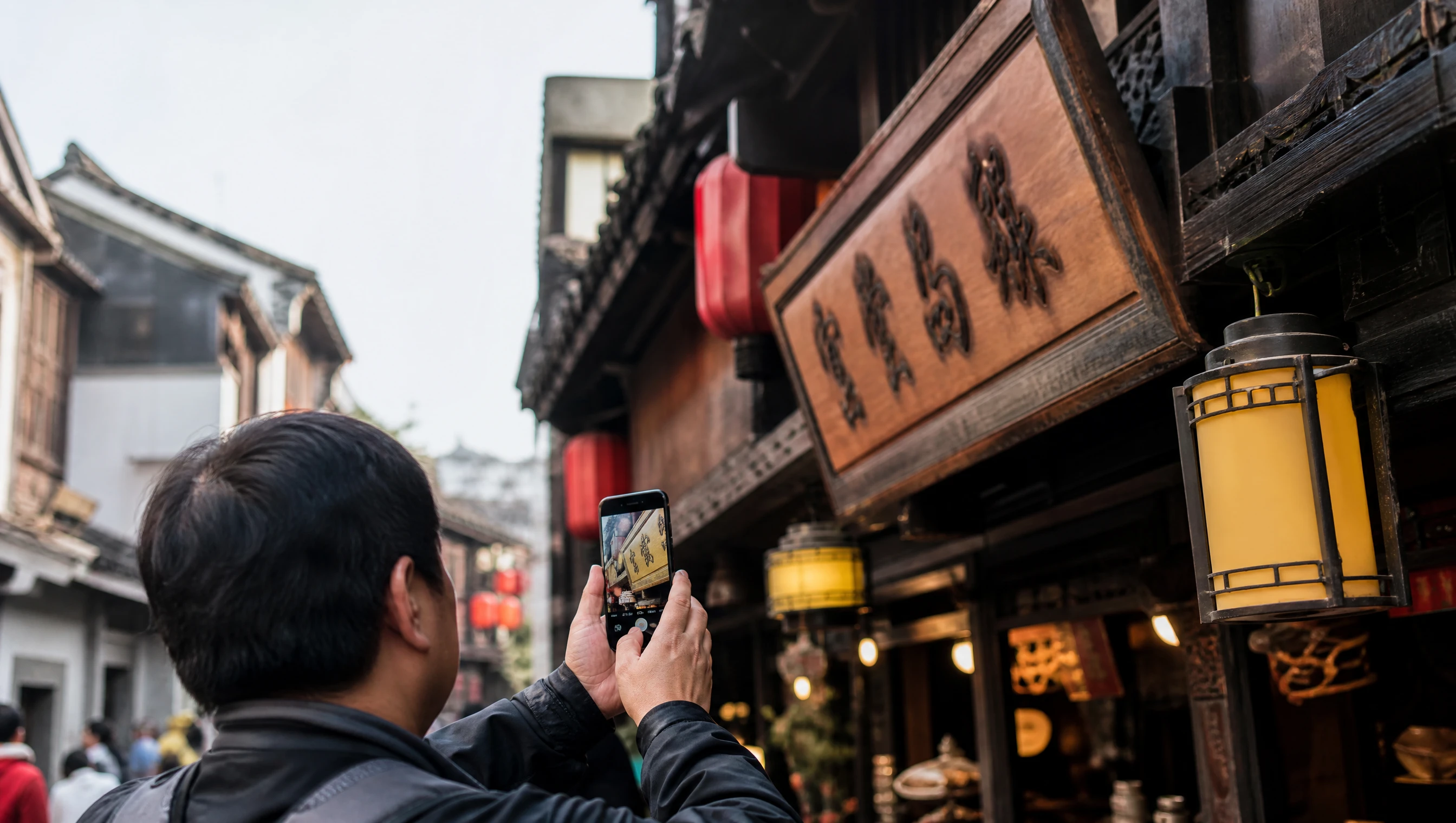 Traveler photographing a shop sign on a lantern-lit old-town street